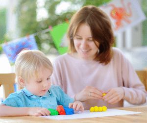 Mother watching child play with playdough at a dining table